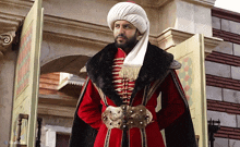 a man wearing a turban and a red coat is standing in front of a door