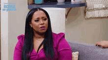 a woman in a pink shirt is sitting on a couch in front of a wall that says house of payne on it