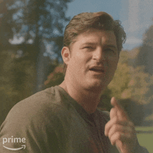 a man in a grey shirt is pointing at the camera with an amazon prime logo behind him