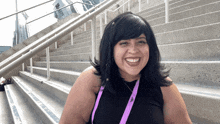 a woman wearing a lanyard with the letter h on it smiles in front of a set of stairs