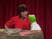 a green kermit the frog kisses a woman on the cheek
