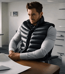 a man is sitting at a desk wearing a black vest