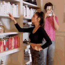 a woman in a black crop top is reaching for a book on a shelf