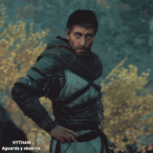 a man in armor stands in front of a tree in a forest