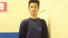 a young man wearing a champion sweatshirt stands in front of a wall .