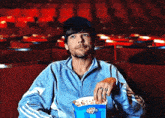 a man in a blue jacket is holding a box of popcorn in a theater .