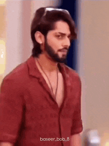 a man with a beard and long hair is wearing a red shirt and a necklace .