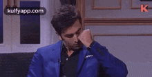 a man in a blue suit is sitting on a couch and talking to someone .