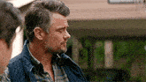 a man with a beard and a plaid shirt is standing in front of a building .