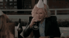 a woman wearing a party hat is sitting at a table drinking a glass of wine