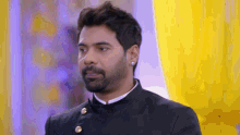 a man with a beard is wearing a black suit and earrings