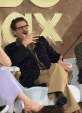 a man in a suit and glasses laughs in front of a fox sign