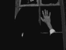 a black and white photo of two hands reaching out of a window