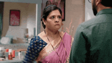a man and a woman are standing next to each other in a room . the woman is wearing a pink saree .