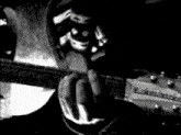 a black and white photo of a person playing a guitar with a skull on the headstock
