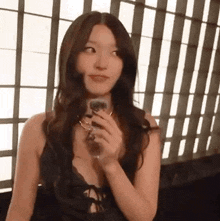 a woman in a black dress is holding a glass of wine and looking at the camera .