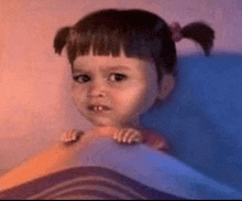 a little girl is laying in bed with her hands on a blanket and making a funny face .