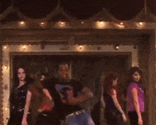 a group of people are dancing in a dark room with a man wearing a black shirt with the letter s on it