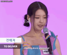a woman in a pink and blue dress is holding a microphone and says " feeling more pressured "