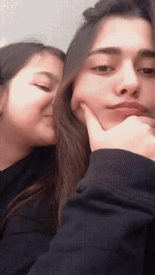a girl kissing another girl on the cheek while holding her hand to her chin