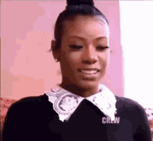 a woman wearing a black shirt with a white collar and a bun is smiling .