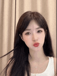 a young woman with long black hair is wearing a white tank top and necklace .