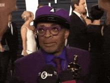 a man in a purple suit is talking into a microphone that says 5live