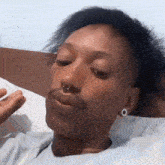 a woman with a nose ring is laying on a bed with her eyes closed