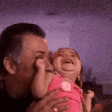 a man is holding a crying baby in his arms and kissing her on the cheek .