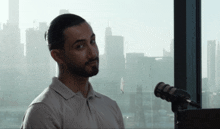 a man with a beard stands in front of a microphone in front of a window