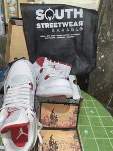 a pair of white sneakers sit on a box next to a south streetwear garage bag