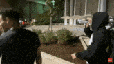 a man in a black hoodie is walking down a sidewalk in front of a building