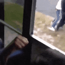 a person 's hand is reaching out to open a window with a person walking in the background