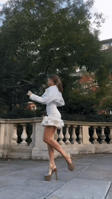 a woman in a white dress and heels is dancing on a sidewalk .