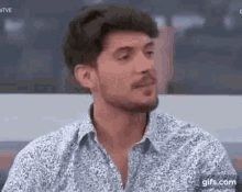 a man with a beard is wearing a floral shirt and talking to someone .