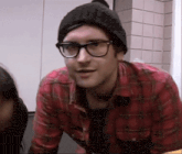 a man wearing glasses and a plaid shirt is looking at the camera