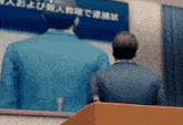 a man in a suit stands at a podium in front of a screen with chinese writing
