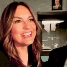 a woman is smiling with a picture of a man on the wall behind her