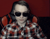 a man wearing sunglasses and a plaid shirt is sitting in a red chair