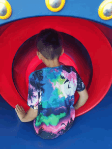 a young boy in a colorful shirt is playing in a red and blue slide