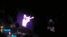 a man in a hat is singing into a microphone in front of a large screen