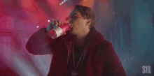 a man in a red jacket and red sunglasses is holding a bottle of pink liquid .