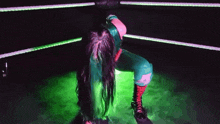 a woman with green hair is kneeling in a ring with green lights behind her