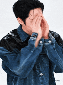 a man wearing a denim jacket covering his face
