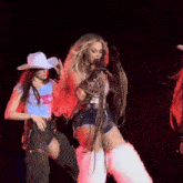 a woman in a cowboy hat is standing next to a woman in shorts and boots