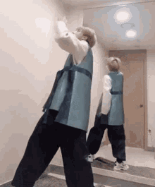 a man in a blue vest and black pants is standing in front of a mirror .