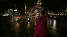 a man in a red cape is walking across a street at night