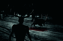 a silhouette of a person with antlers walking in the dark