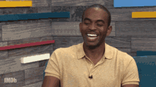 a man in a yellow shirt is laughing in front of a wall that says imdb on it