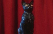 a statue of a cat with glowing eyes is sitting in front of a red curtain